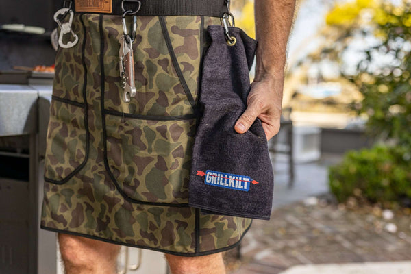 man with grillkilt towel in hand and lots of grilling accessories. grillkilt the ultimate grilling apron