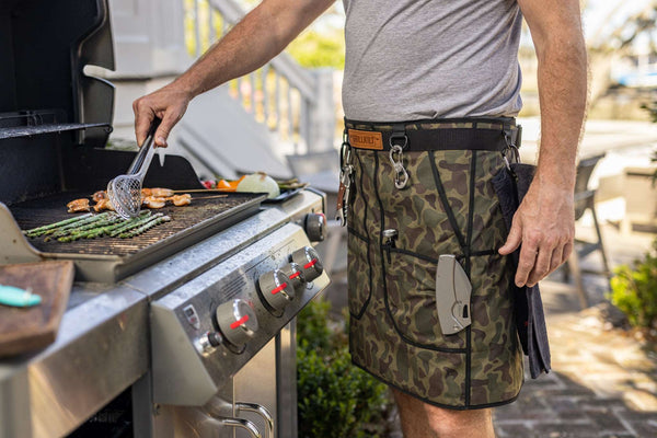 Person grilling in a Vintage Camouflage GRILL KILT apron with pockets by a grill