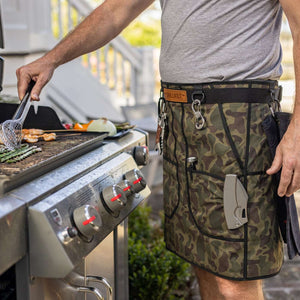 Person grilling in a Vintage Camouflage GRILL KILT apron with pockets by a grill